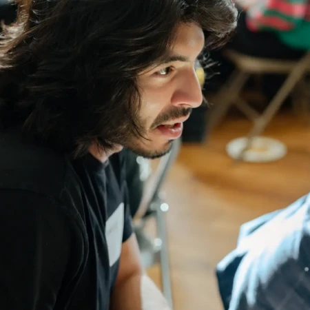 Person with long dark hair speaking during a collaborative workshop session, seated in a light-filled event space.